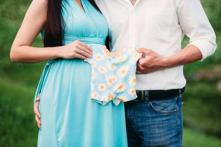 future paremts holding kids clothes near pregnant belly. Family conceptの写真素材