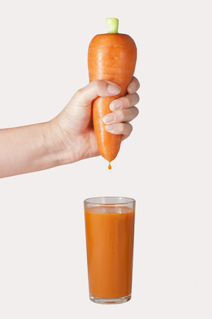 A woman's hand squeezes fresh juice. Pure carrot juice pouring out from fruit into glassの写真素材