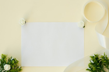 Workspace. Wedding invitation card, satin ribbon, white roses and green leaves on beige background. Overhead view. Flat lay, top view wedding invitation card Templatesの写真素材