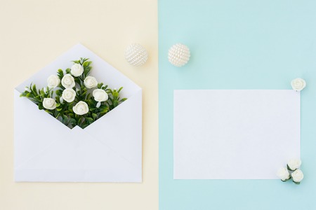 Workspace. Wedding invitation card, envelope, white roses and green leaves on beige blue background. Overhead view. Flat lay, top view wedding invitation card Templatesの写真素材
