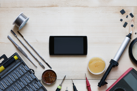 Repairman workplace with smartphone and special tools. Tool kit: multimeter, magnifying glass, soldering iron, rosin, tin, tweezers, screwdrivers, blades, tin pump. Electronics repair service. Place for your text, copy spase mockupの写真素材