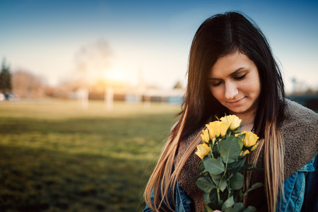 Attractive young woman with yellow rose in the parkの写真素材
