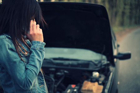 Young caucasian woman with brown hair under the hood of her car break downの写真素材