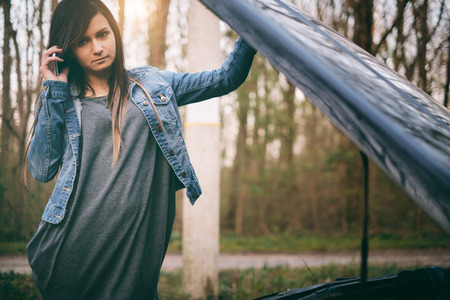 Young caucasian woman with brown hair under the hood of her car break downの写真素材