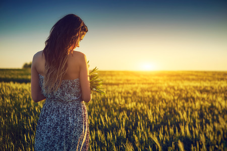 Young woman on wheat field holding white flowerの写真素材