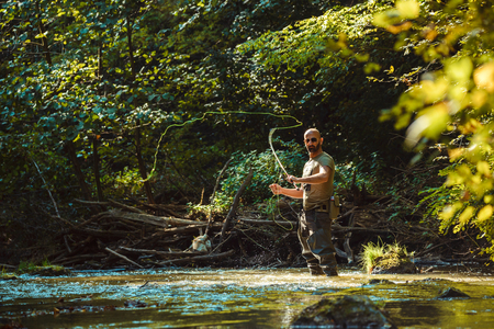 A fisherman fishing with fly fishing in the flowing streamの写真素材