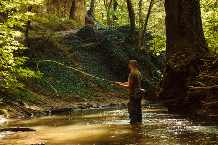 A fisherman fishing with fly fishing in the flowing streamの写真素材