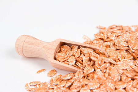 Pile of wheat flakes with wooden scoop isolated on white