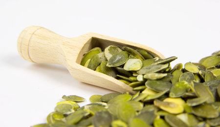 Pile of pumpkin seeds with wooden scoop isolated on whiteの写真素材