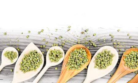 Photo of spoons with green pepper seeds on wooden board with white space for textの写真素材