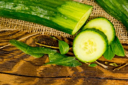 Photo of cucumber, slices and leaves on burlap and wooden boardの写真素材