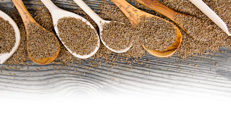 Photo of spoons with cumin seeds on wooden board with white space for text