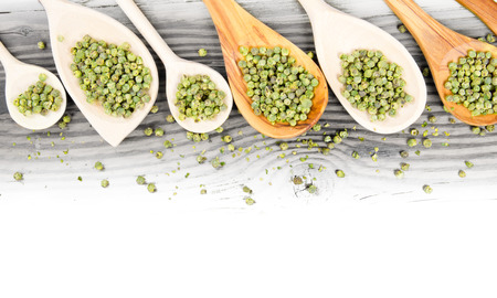 Photo of spoons with green pepper seeds on wooden board with white space for textの写真素材
