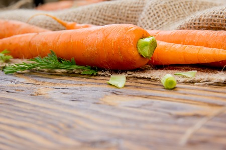 Photo of carrots with leaf on burlap and wooden boardの写真素材