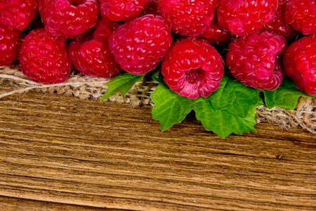Photo of raspberries with leaves on burlap and wooden boardの写真素材