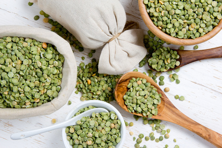 Top view of spoons and bowls full of green lentil seeds on white wooden surfaceの写真素材