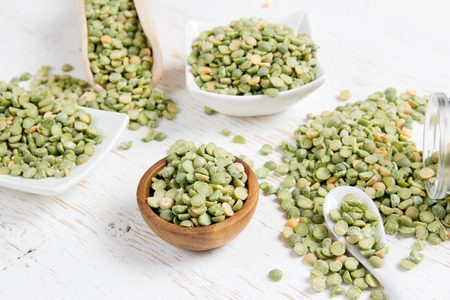 Photo of bowls full of green pea seeds on white wooden surface