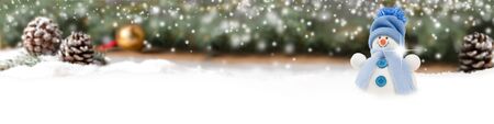 Wide horizontal composition of single blue snowman on spruce branch and cone background with...
