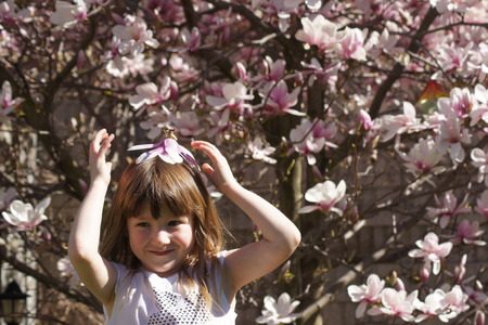 Pretty little girl in front of magnolia tree with flower on her head.の写真素材