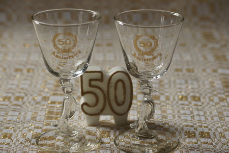 50th anniversary glasses and candle, gold and white table cloth background.の写真素材