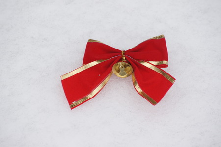 Red bow with gold trim and gold bell with snow white background.の写真素材