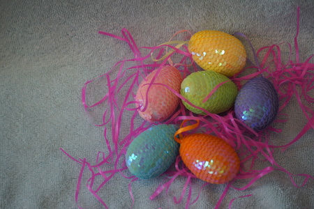 Several bright and shiny Easter eggs lay in the midst of bright pink straw.