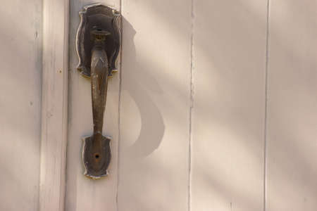 Antique beautiful door handle on an aged wooden door painted white.の写真素材