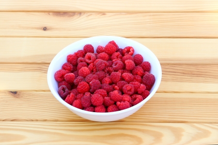 Fresh raspberries in a round white plate on a wooden tableの写真素材