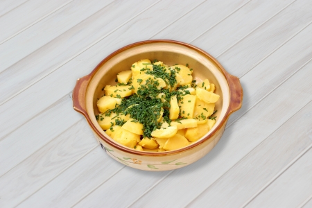 Greek potato salad with dill in a bowl on a white wooden tableの写真素材
