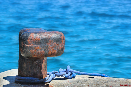 Old rusty mooring bollard on concrete pier with ropeの写真素材