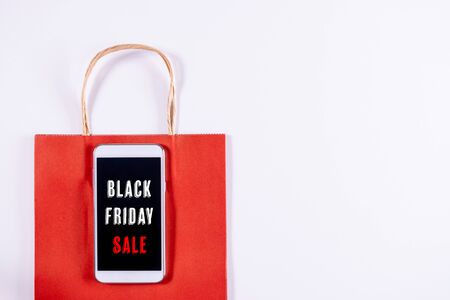 Black Friday concept. Mobile phone or smartphone with paper bag on white background. Online shopping.の写真素材