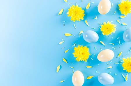 Easter eggs in pastel colors and yellow flower on pastel blue sky background.
