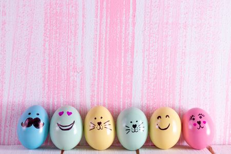 Row of hand painted Easter eggs over pastel pink wooden background.