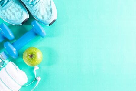 Healthy lifestyle, food and sport concept. Fitness equipment. Sneakers, water, dumbbells and headphones on pastel blue sky background.の写真素材