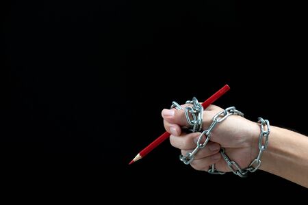 Hand with red pencil tied with fetters, depicting the idea of freedom of the press or freedom of...