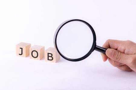 Close-up wooden blocks with text JOB sign and woman hand holding magnifying glass on white background. Recuriting concept. Copy space for advertisers or background.の写真素材
