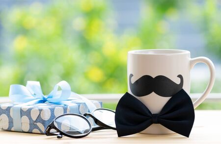 Happy fathers day concept. beautiful gift box, glasses and coffee cup with black mustache on wooden table over green bokeh background.の写真素材