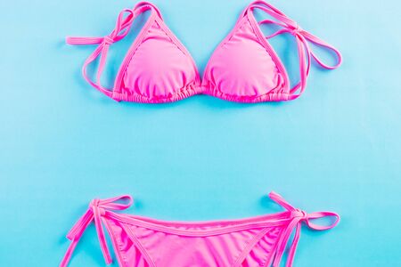 Sexy pink bikini  on light blue background. Top view flat lay, hipster beach clothes, chic swimsuit, summer vacation concept, pink bra close-up. Copy space for advertisers.の写真素材