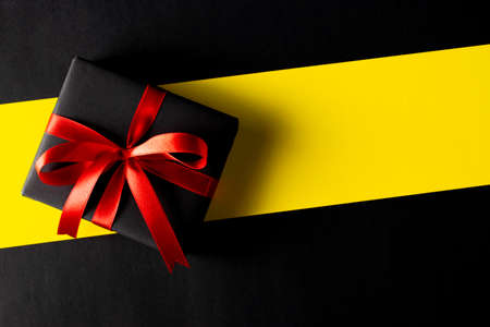 Top view of black christmas boxes with red ribbon on Yellow background with copy space for text. Cyber Monday composition or Black Friday, Boxing Day.の写真素材