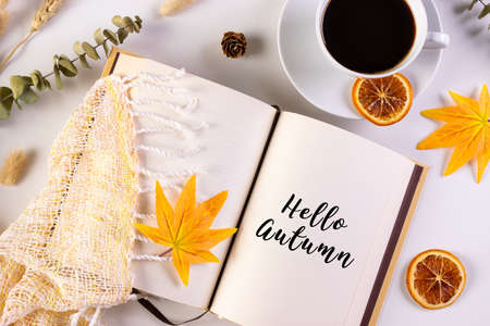 Autumn leaves, cup of coffee, book reading warm scarf and opened book on the table with text Hello Autumn. Fall and autumn concept.の写真素材