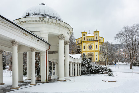Marianske Lazne, Czech Republic - December 29 2020: Winter scenery of Christian church of the assumption of Mary and Rudolph and Caroline spring colonnade in Marienbad covered with white snow.のeditorial素材