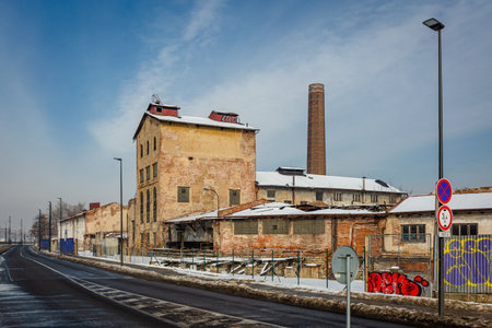 Prague, Czech Republic - February 16 2021: Former distillery called Lihovar, a ruined building made of bricks, a chimney and a road with traffic signs and lamps. A sunny winter day with clouds.のeditorial素材
