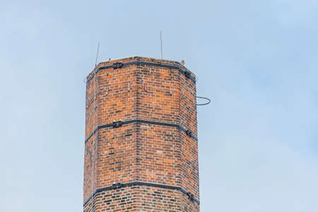 Chimney made of red bricks and a kestrel sitting on the top. Sunny winter day with clear blue sky in the background.の写真素材