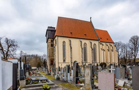 Milevsko, Czech Republic - February 27 2021: View of the medieval roman catholic church of St Giles standing in the middle of the graveyard. Winter day with cloudy blue sky.のeditorial素材
