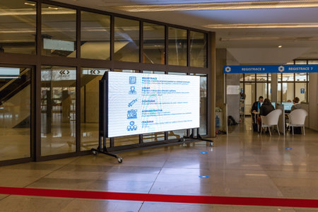 Prague, Czech Republic - March 26 2021: View of the interior of the Metropolitan vaccination center - COVID-19 at Prague Congress center. Big screen with text. People sitting at registration deskのeditorial素材
