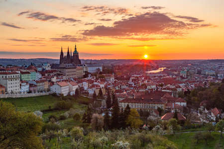 Prague, Czech Republic - May 3 2021: Colorful sunrise view of the city from Petrin hill with the castle, garden, trees, river and buildings. Clouds on the yellow, orange, pink and blue sky.のeditorial素材