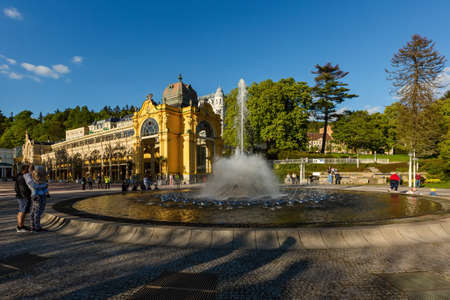 Marianske Lazne, Czech Republic - May 30 2021: View of the spurting water fountain. Yellow colonnade building in the background. Sunny spring day in a spa city.のeditorial素材