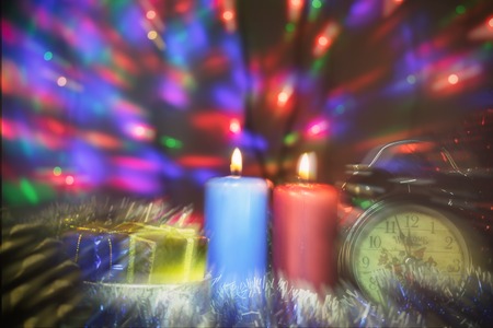 two candles with clock and Christmas gifts with multi-colored lights on background blurred double focus imageの写真素材