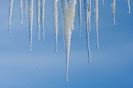 Icicles hanging from an eave against a brilliant blue skyの写真素材