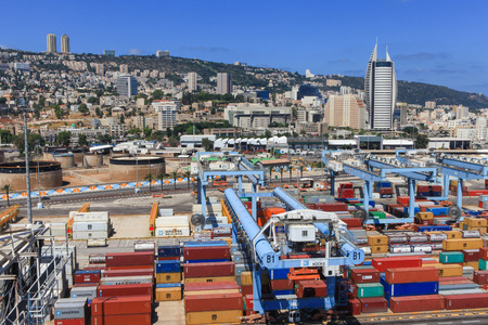 Haifa, Israel - July 10, 2015: Various brands and colors of shipping containers stacked in a holding platform waiting for loading with the city of Haifa in the backgroundのeditorial素材